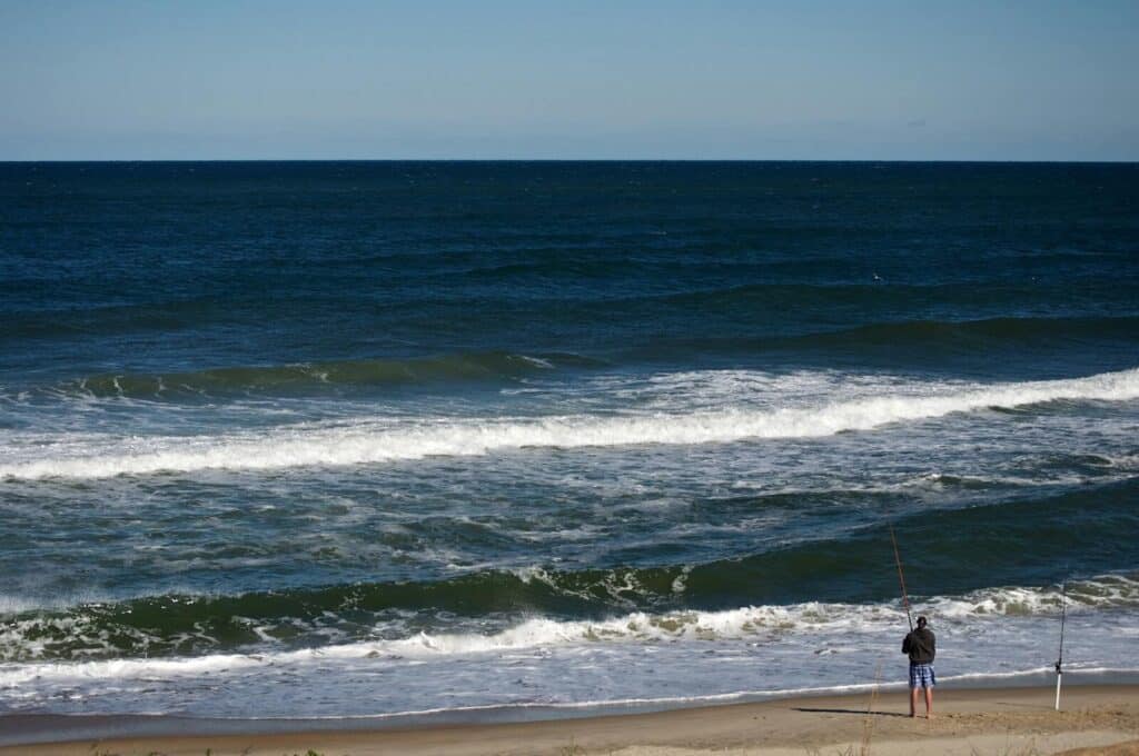 A lone fisherman casts a line on Nags Head beach, North Carolina, with waves crashing on the shore.