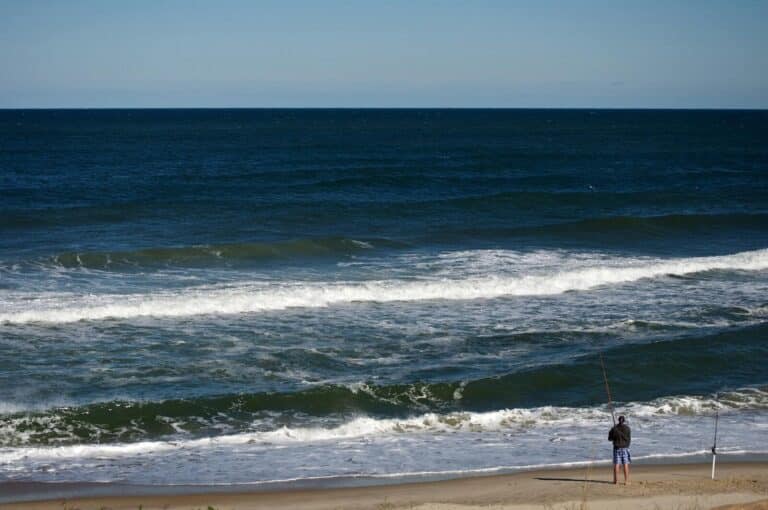 A lone fisherman casts a line on Nags Head beach, North Carolina, with waves crashing on the shore.