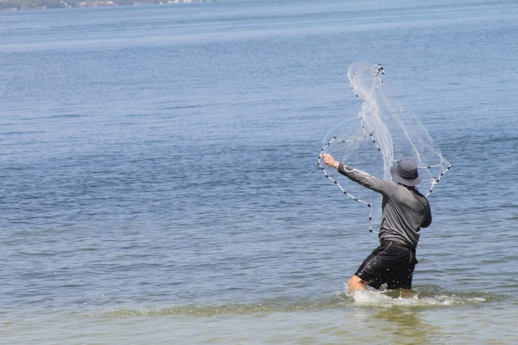 An angler throwing a cast net over shallow water for bait