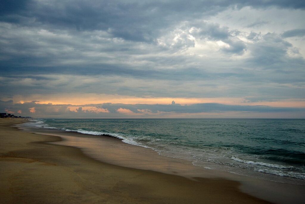 Peaceful beach scene at sunset in Kitty Hawk, North Carolina with dramatic sky.