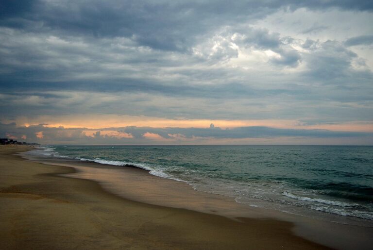 Peaceful beach scene at sunset in Kitty Hawk, North Carolina with dramatic sky.