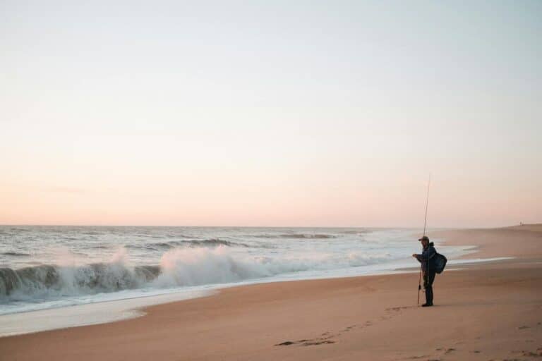 A lone fisherman casting on a serene beach at sunset, offering tranquility and solitude.