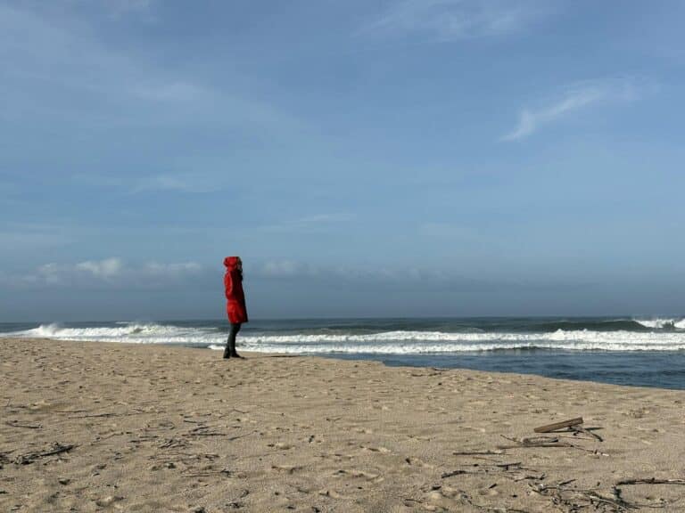 A lone angler in a red coat walks the empty winter beach on the Outer Banks