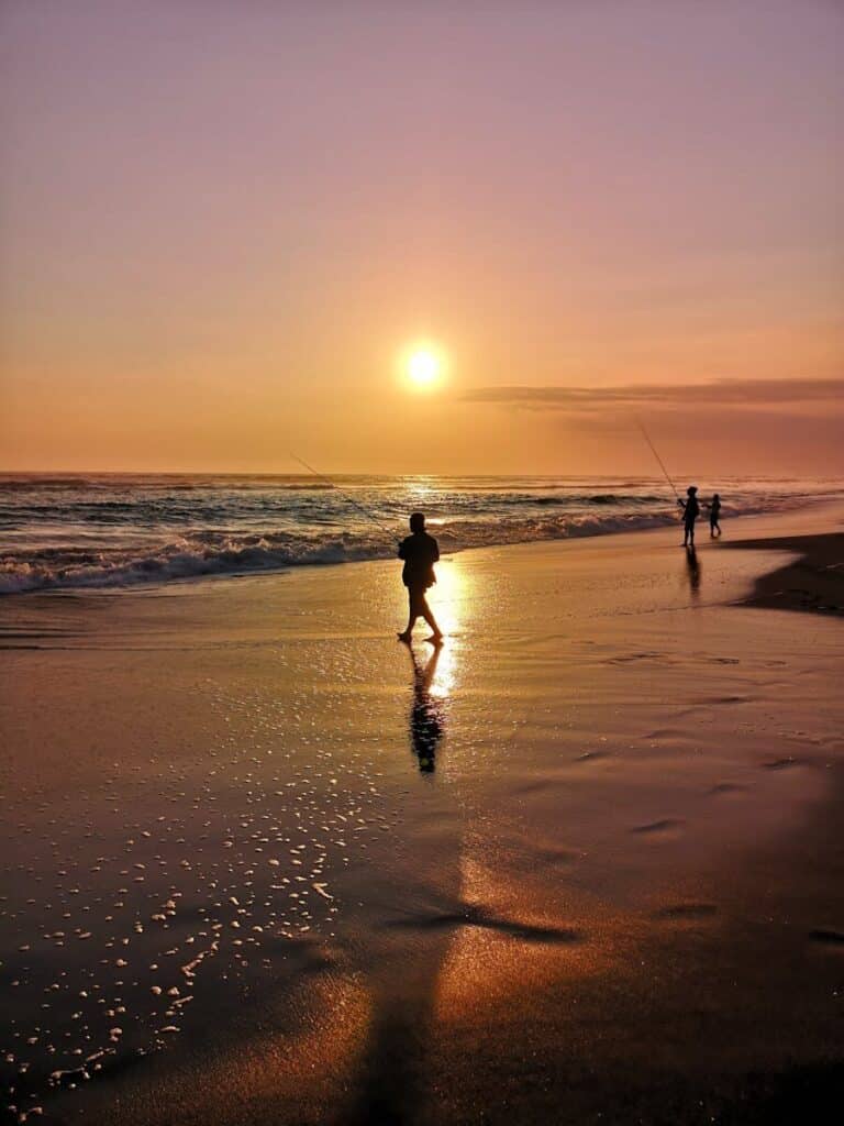 Peaceful sunrise at the beach with silhouettes of fishermen casting lines into the ocean.