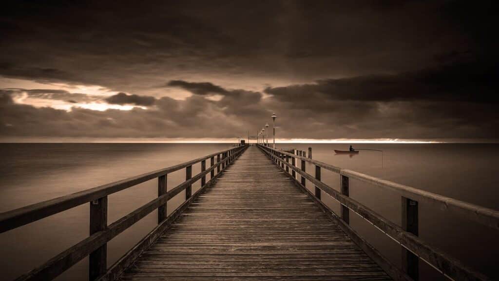 Silhouette of a fisherman casting from an Outer Banks pier at sunset, with the sun setting over the ocean horizon.