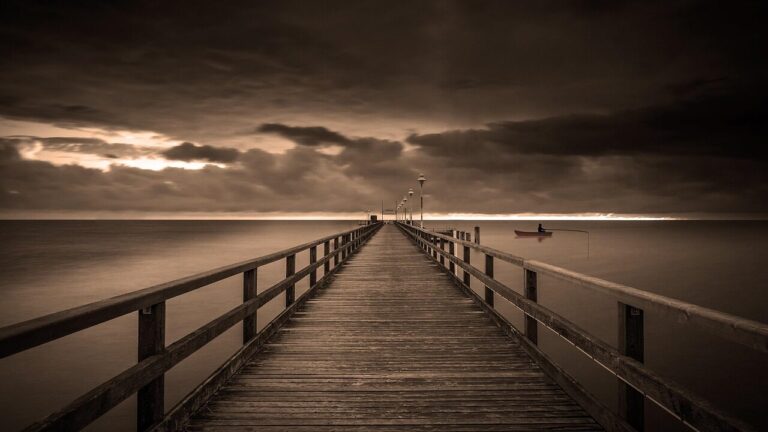 Silhouette of a fisherman casting from an Outer Banks pier at sunset, with the sun setting over the ocean horizon.