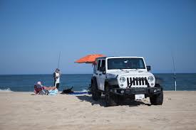 Outer Banks fishing without a charter — a Jeep parked on the beach with surf rods and an umbrella by the ocean