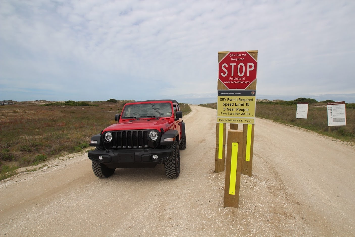 Red Jeep Wrangler parked at a Cape Hatteras National Seashore ORV permit sign on an Outer Banks beach access