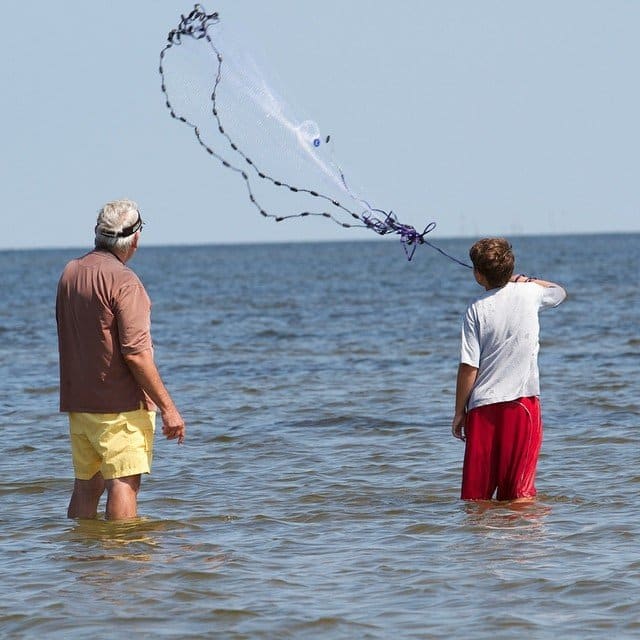 Two people throwing a cast net for bait fish in shallow water at Cape Hatteras