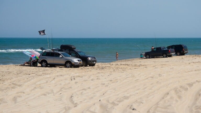 Four-wheel-drive vehicles parked on the sand with a fishing rod and flag beside the ocean