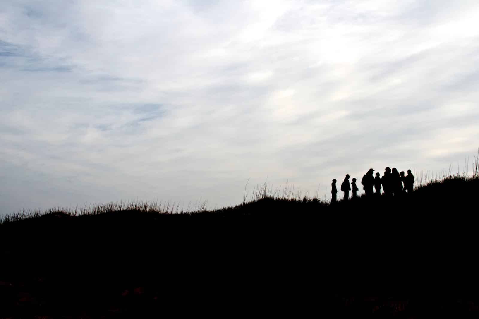 People silhouetted on top of a dune against a cloudy sky at Cape Hatteras National Seashore