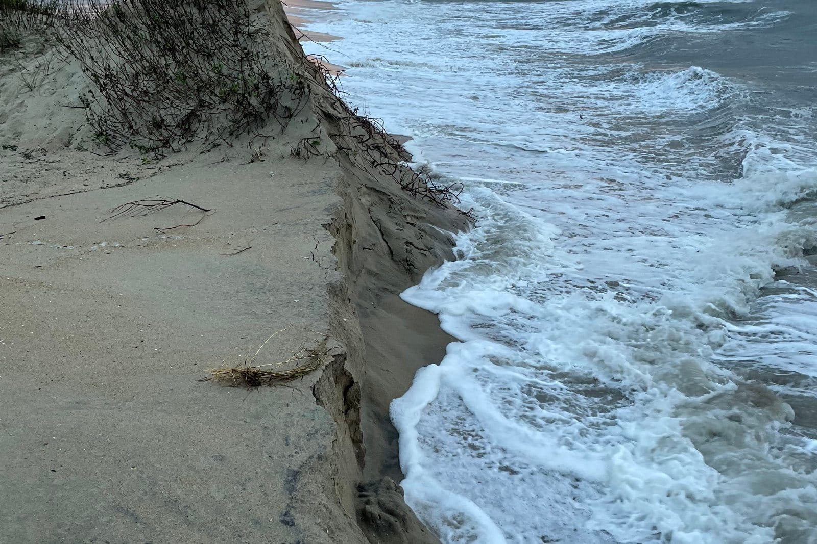 Surf breaking against a steep eroded dune scarp at the end of the bypass road south of Ramp 44 near Cape Point