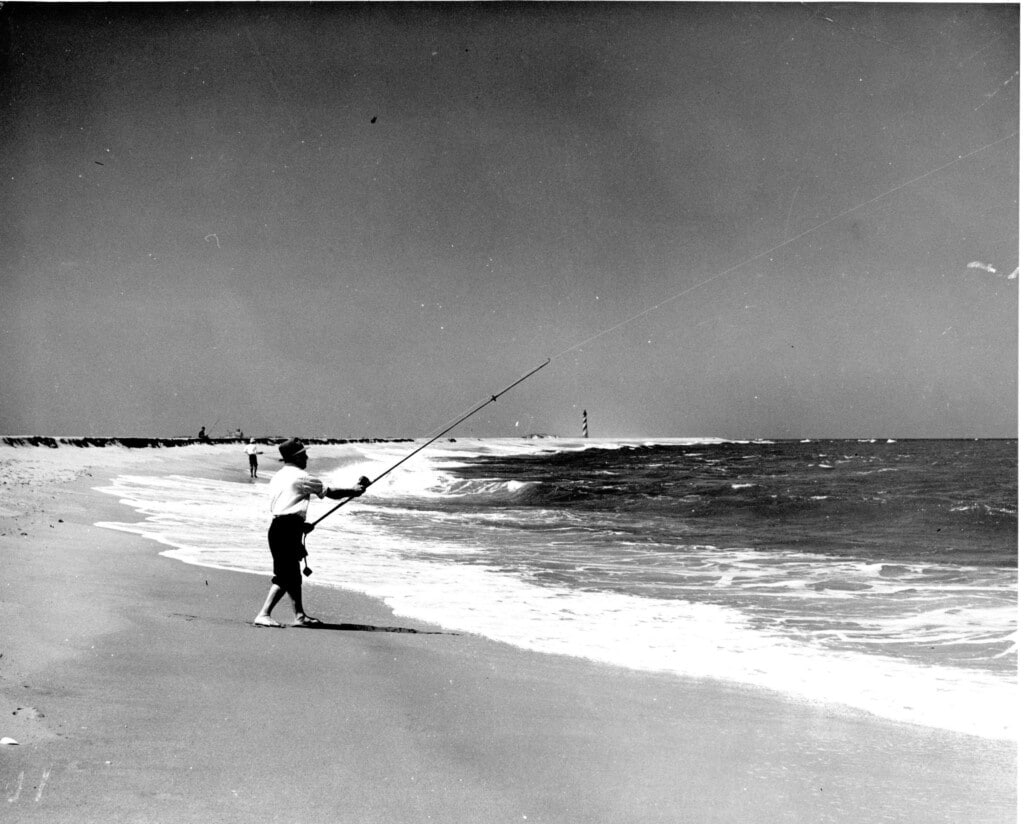 Black and white 1952 photograph of a man surf fishing on the beach south of Cape Hatteras Lighthouse