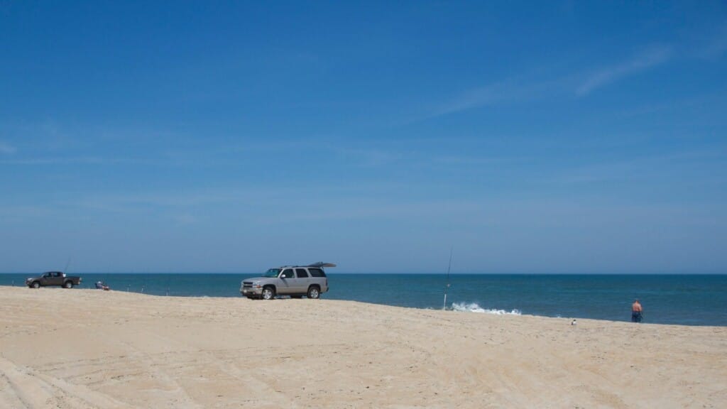 Anglers and beach vehicles spread along a wide Outer Banks beach under a deep blue sky