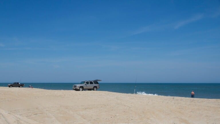 Anglers and beach vehicles spread along a wide Outer Banks beach under a deep blue sky