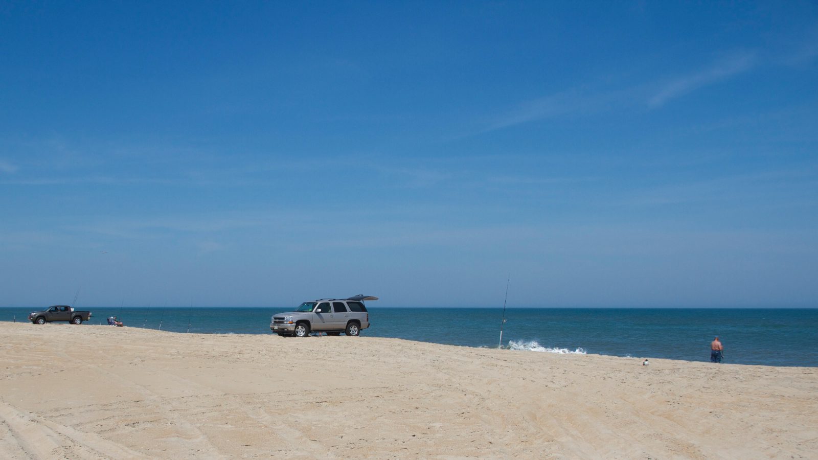Anglers and beach vehicles spread along a wide Outer Banks beach under a deep blue sky