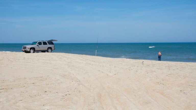 A surf angler fishing beside a beach vehicle on the shoreline at Cape Hatteras National Seashore