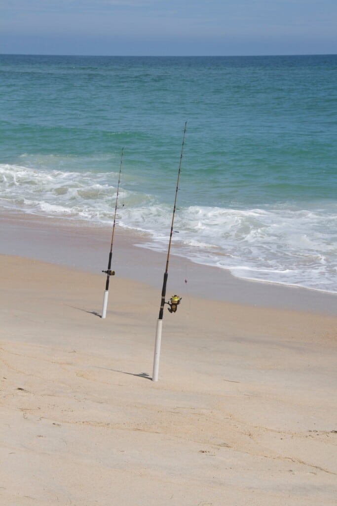 Two surf fishing rods standing in sand spikes at the edge of the breaking surf
