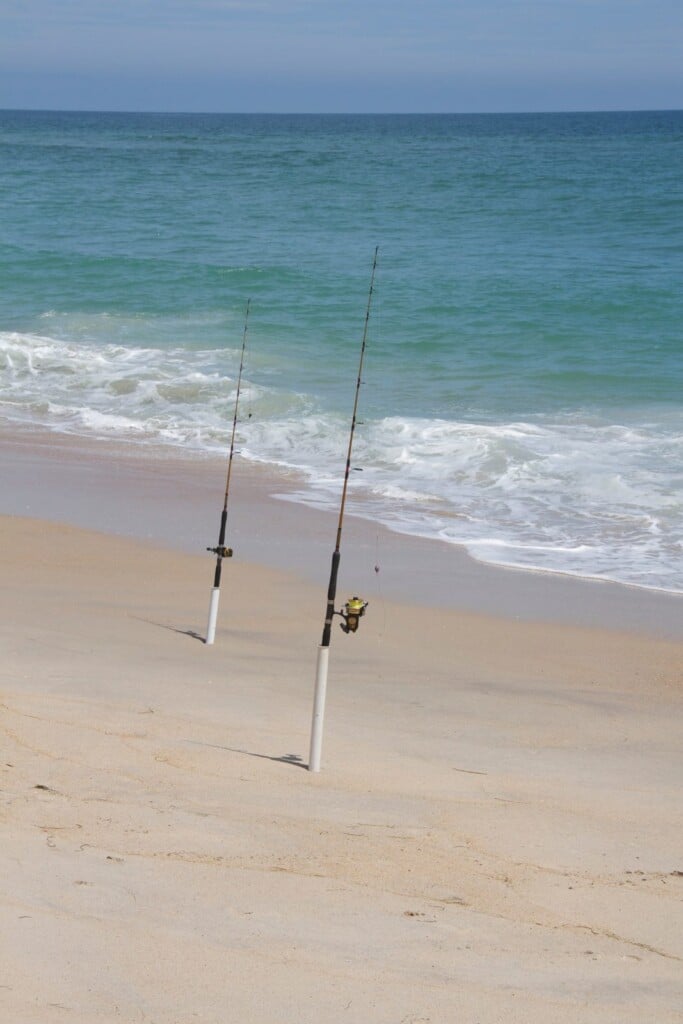 Two surf fishing rods standing in sand spikes at the edge of the surf on an Outer Banks beach