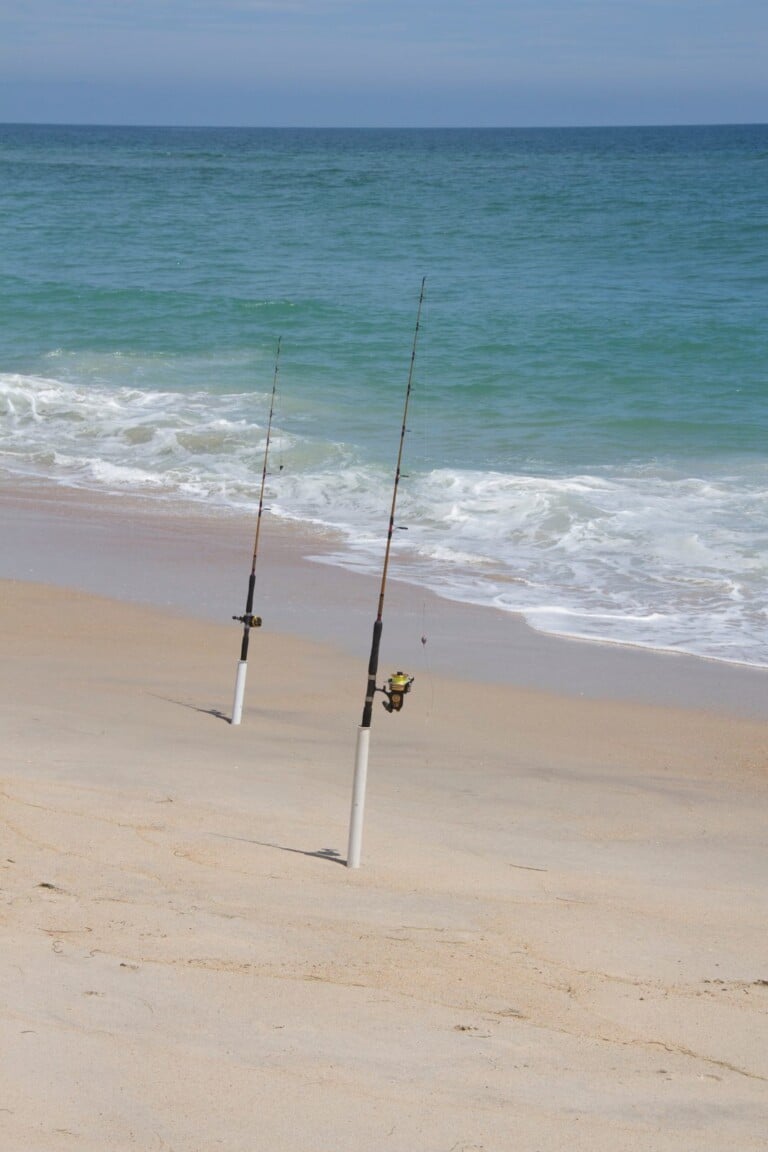 Two surf fishing rods standing in sand spikes at the edge of the surf on an Outer Banks beach