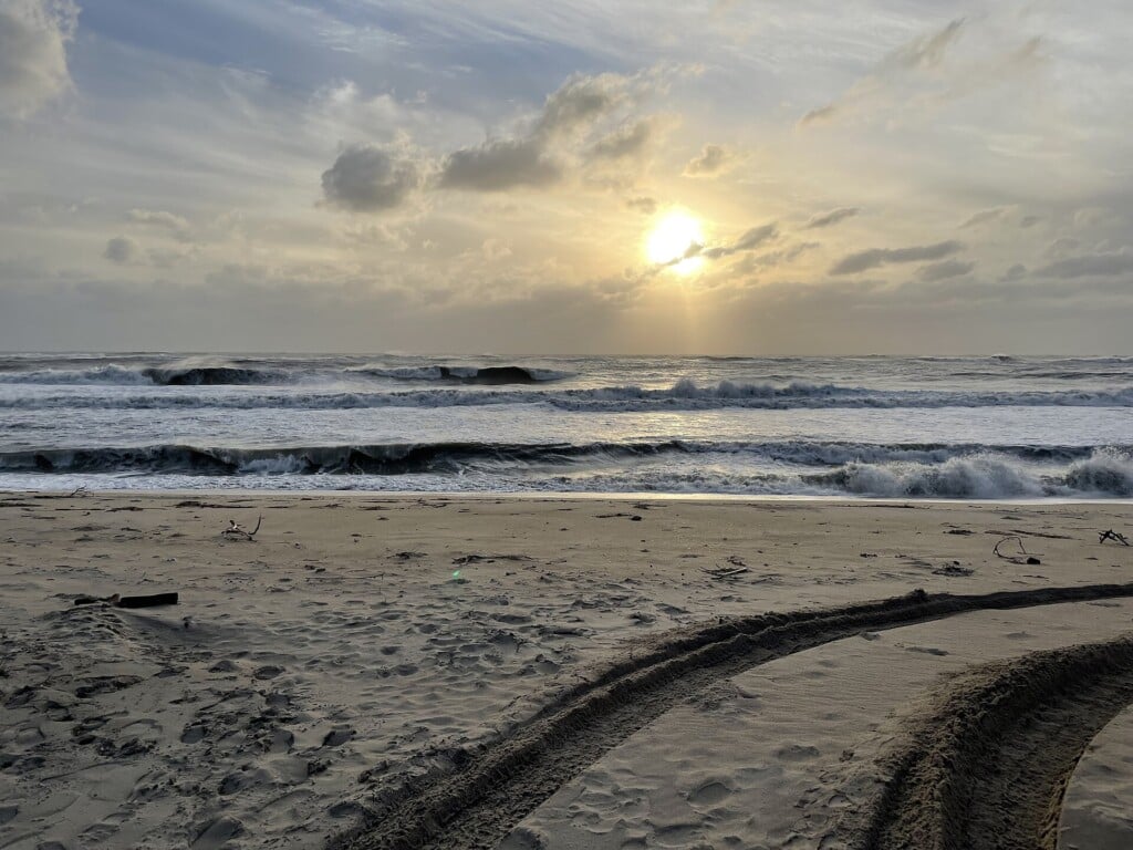 Sunrise over the ocean at Cape Point with tire tracks in the sand
