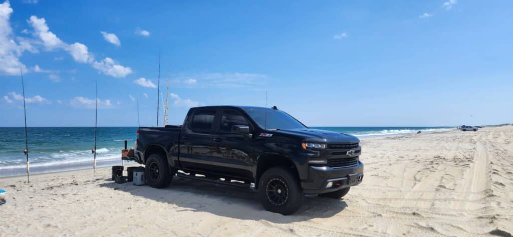 A black Chevy Silverado Z71 pickup parked on the beach with surf rods standing in sand spikes