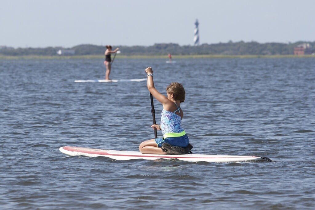 A paddleboarder on the Pamlico Sound with the Cape Hatteras Lighthouse in the distance