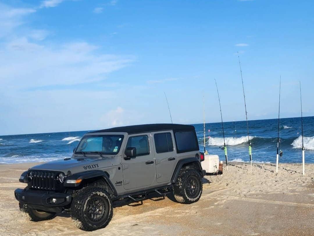 A gray Beach4x4 Jeep Wrangler Willys on the Outer Banks beach with surf fishing rods set in sand spikes